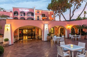 A hotel with a pink facade, outdoor seating area, and a sign reading "San Valentino". - Hotel San Valentino (Ischia)