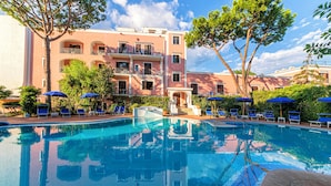 A swimming pool with lounge chairs and umbrellas, surrounded by a building with balconies and trees. - Hotel San Valentino (Ischia)