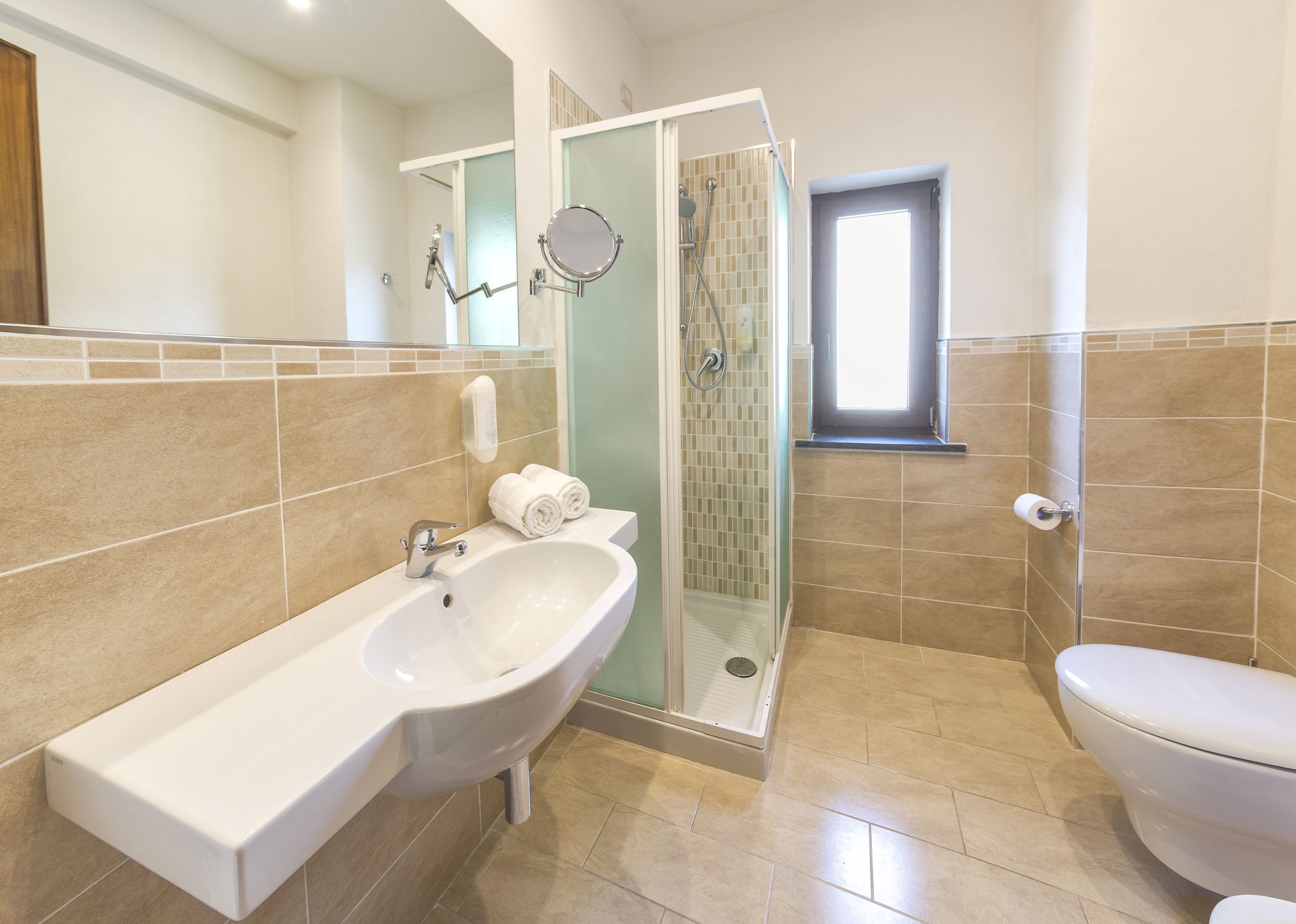 Un baño con lavamanos blanco, ducha con mampara de vidrio y un inodoro.