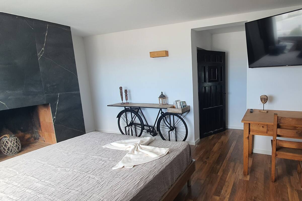 Une chambre à coucher avec un lit, un bureau en bois, une télévision et un vélo.