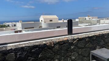 En takterrass med en stenmur, en svart högtalare och utsikt över havet och byggnaderna.