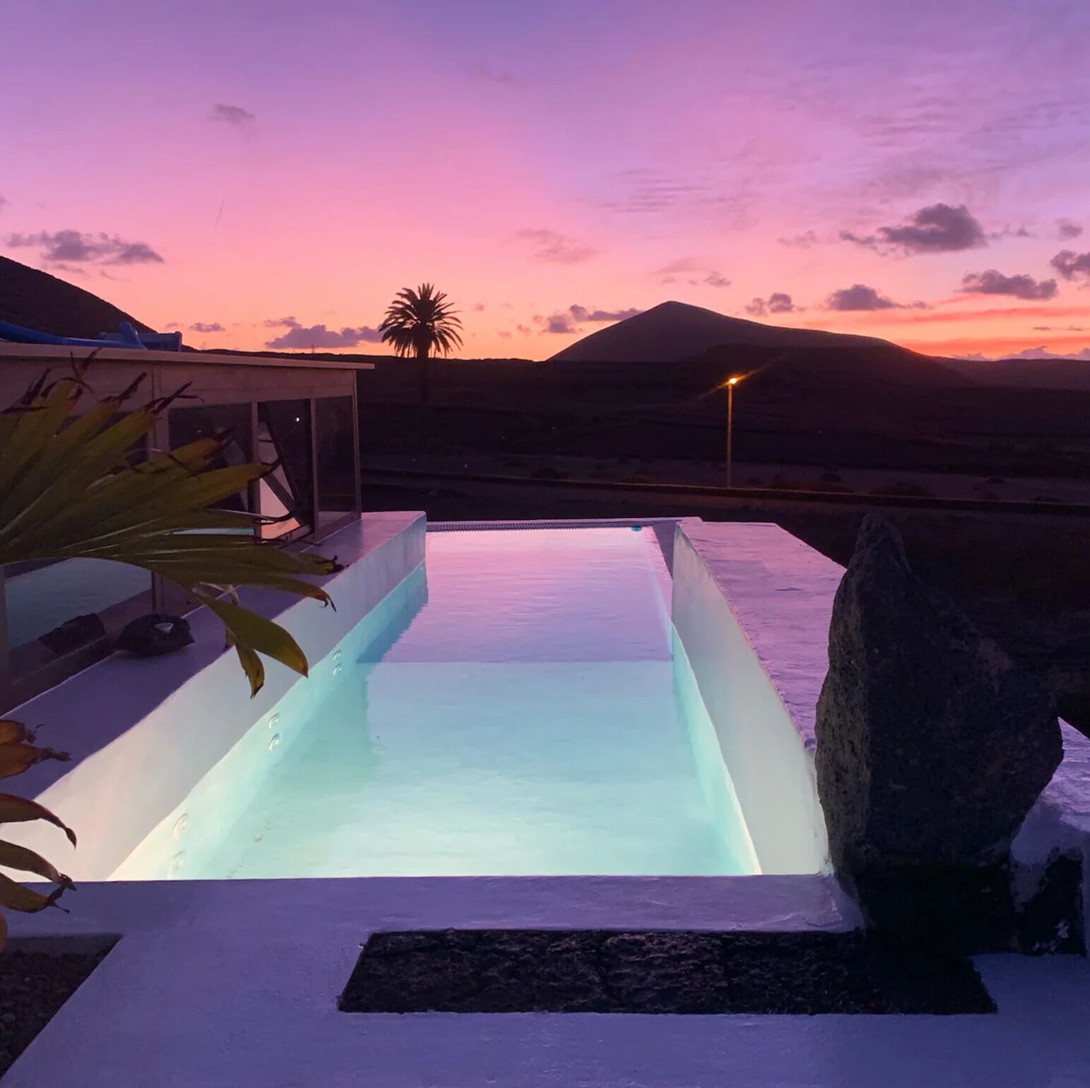 A modern pool area with a clear view of the sunset and mountains in the background.