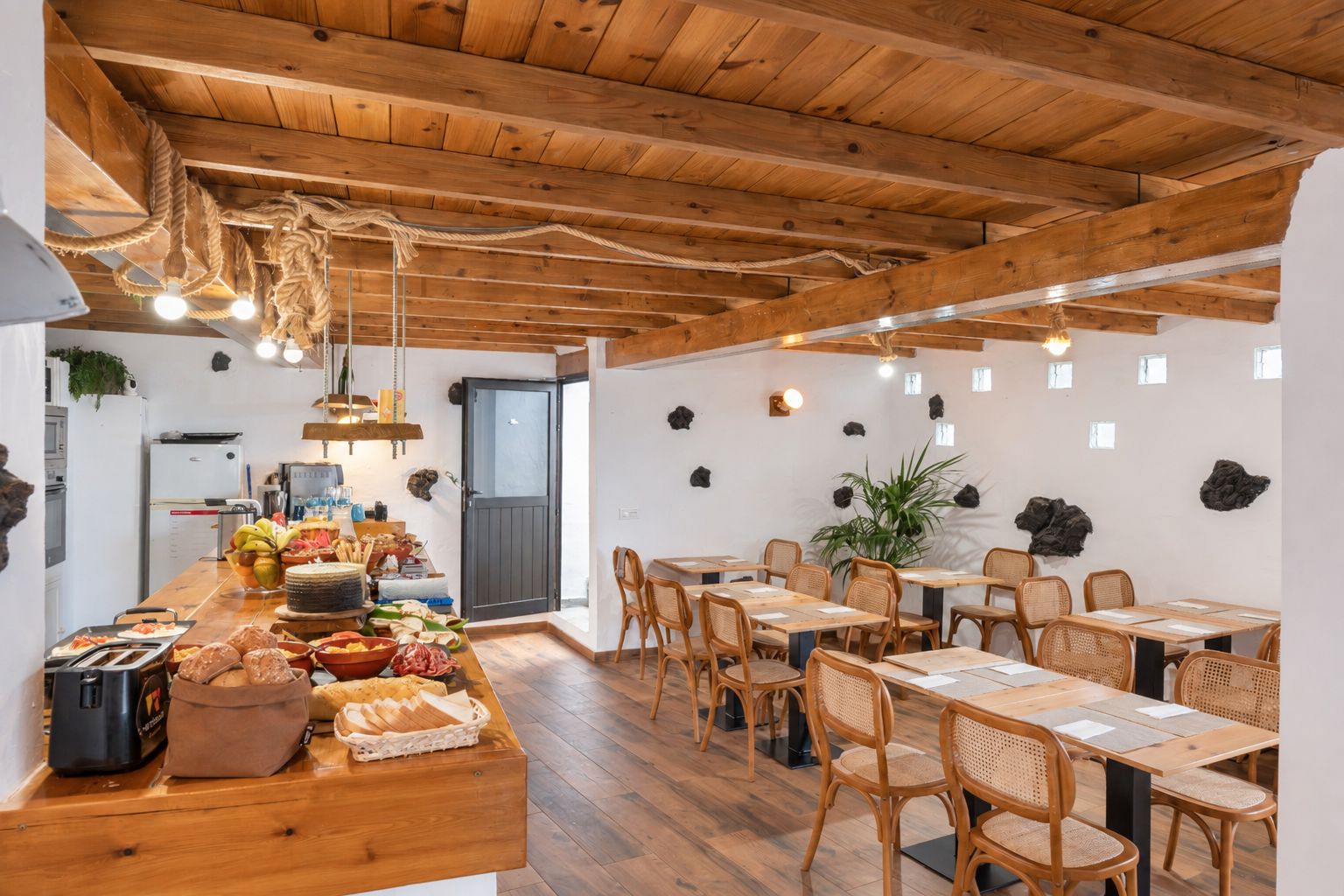 A dining area with wooden tables and chairs, a buffet counter with food items, and a ceiling with exposed beams.