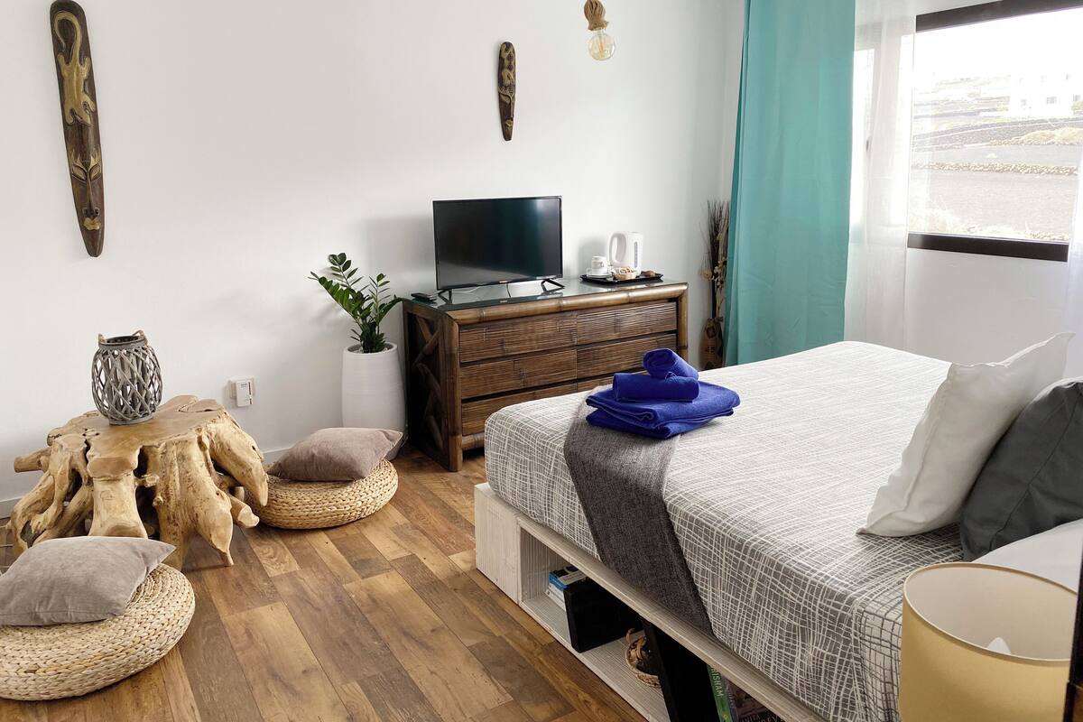 Une chambre moderne avec un lit en bois, une télévision, une commode et une fenêtre avec des rideaux.