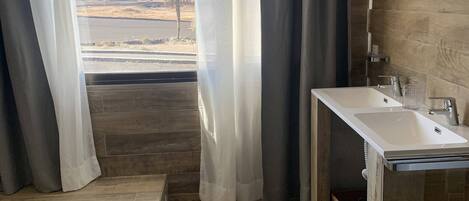 A modern bathroom with a wooden floor, a large window with curtains, and a sink.