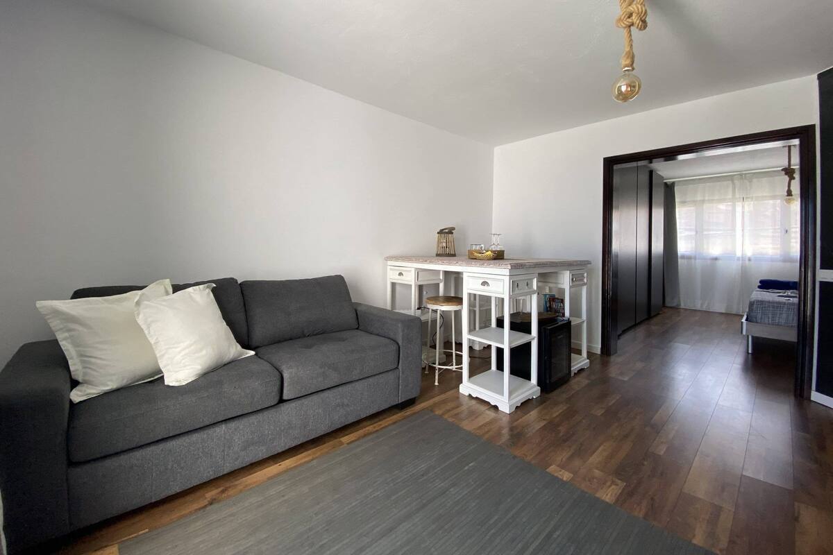 Un salon moderne avec un canapé gris, des tables d’appoint blanches et un plancher en bois.