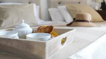 A neatly arranged breakfast tray with croissants and a cup, set on a bed with white linens and a hat on the pillow.