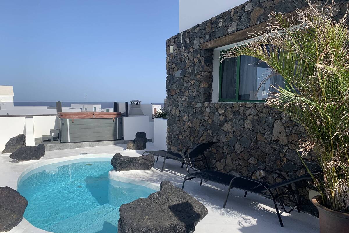 Une piscine sur le toit offrant une vue dégagée sur la mer, entourée de murs en pierre et agrémentée de quelques chaises longues.