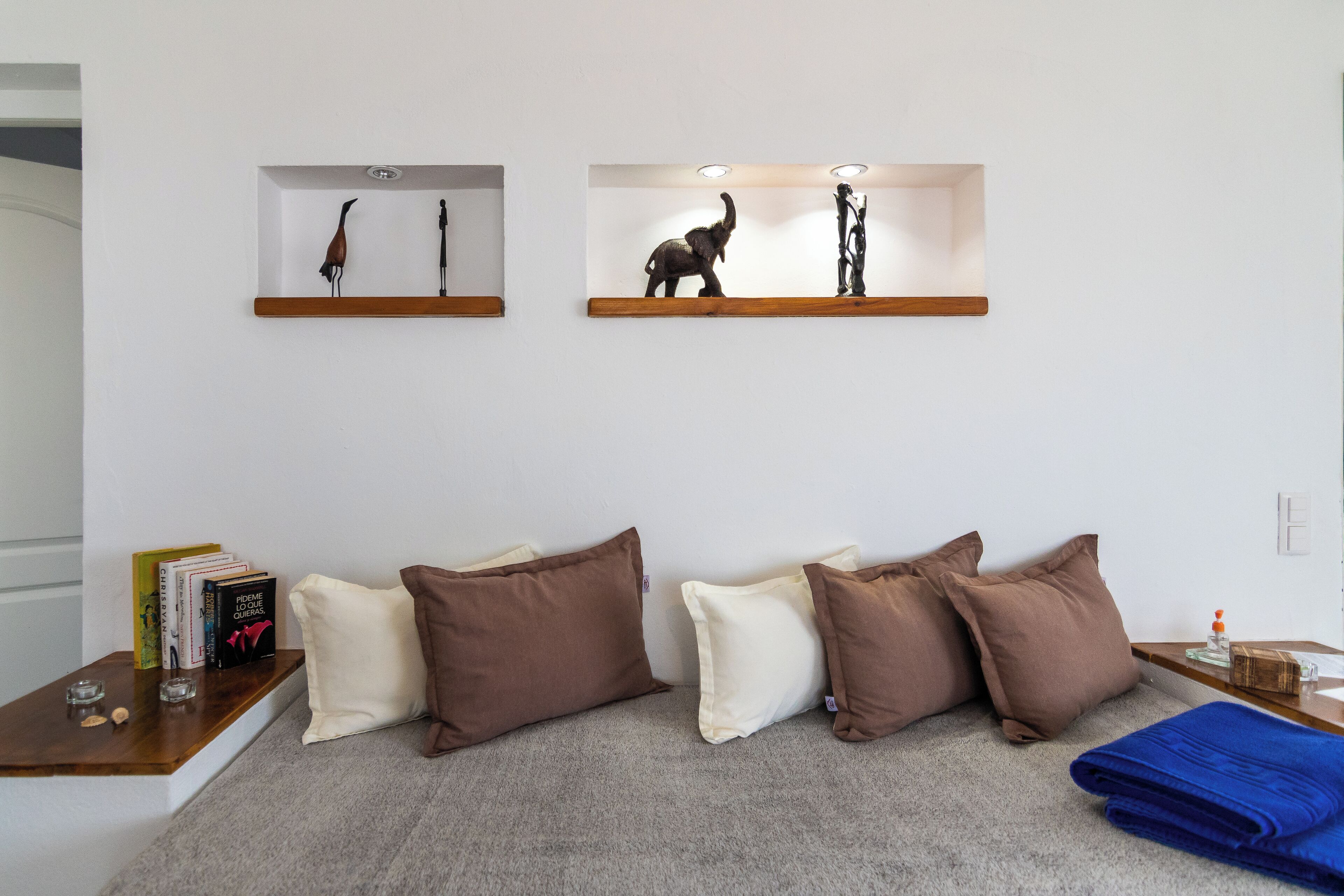 Una sala de estar moderna con un sofá, almohadones, una mesa de centro y dos estanterías con esculturas.