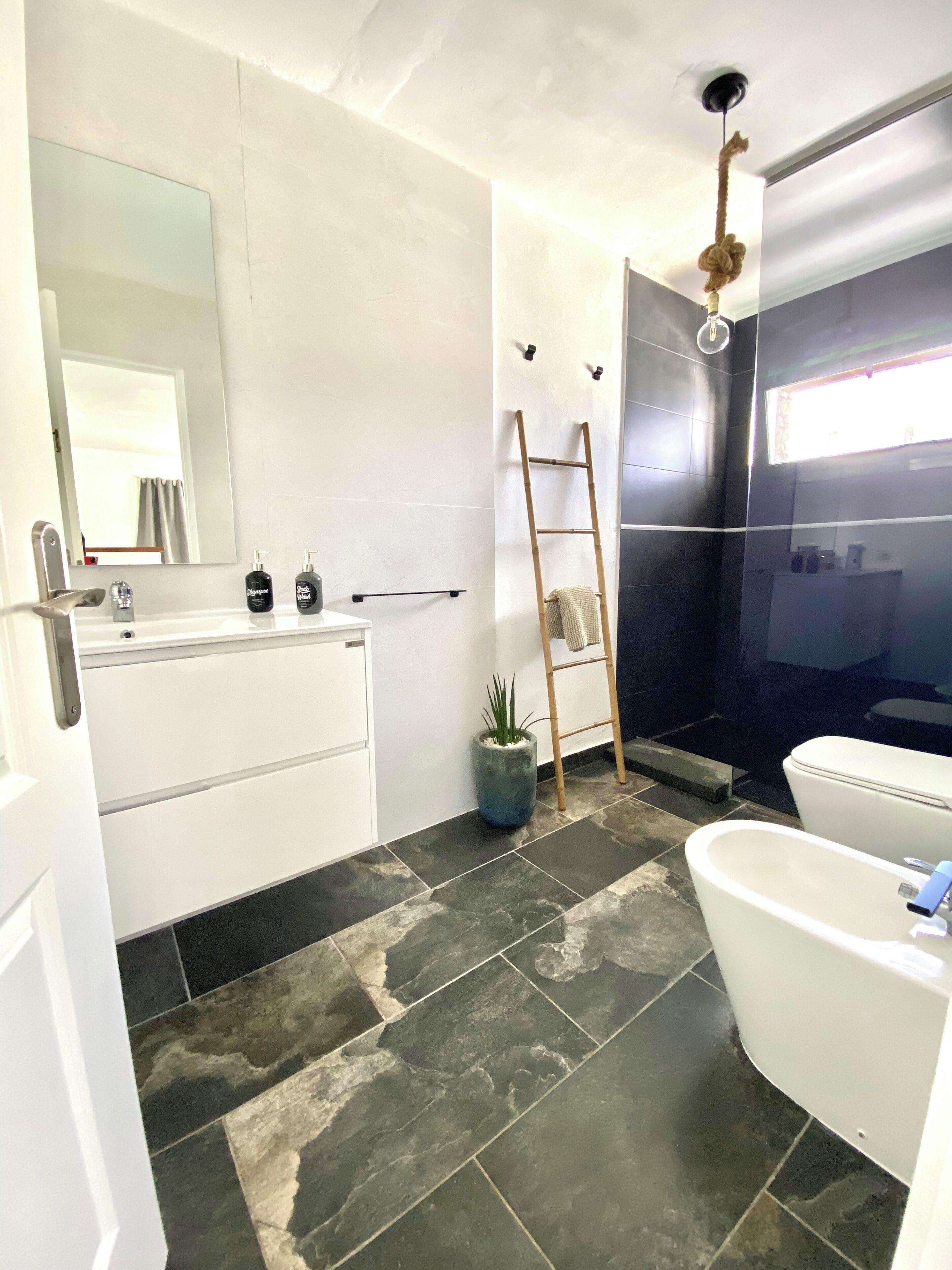 Un baño moderno con una bañera blanca, un espejo grande, un lavabo con artículos de tocador, una planta en maceta y una zona de ducha.