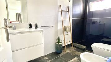 Un baño moderno con una bañera blanca, un espejo grande, un lavabo con artículos de tocador, una planta en maceta y una zona de ducha.