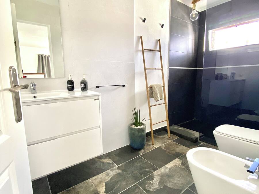 Un baño moderno con una bañera blanca, un espejo grande, un lavabo con artículos de tocador, una planta en maceta y una zona de ducha.