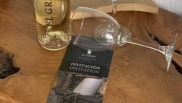A bottle of El Grifo wine, a glass, and an invitation card on a wooden surface.