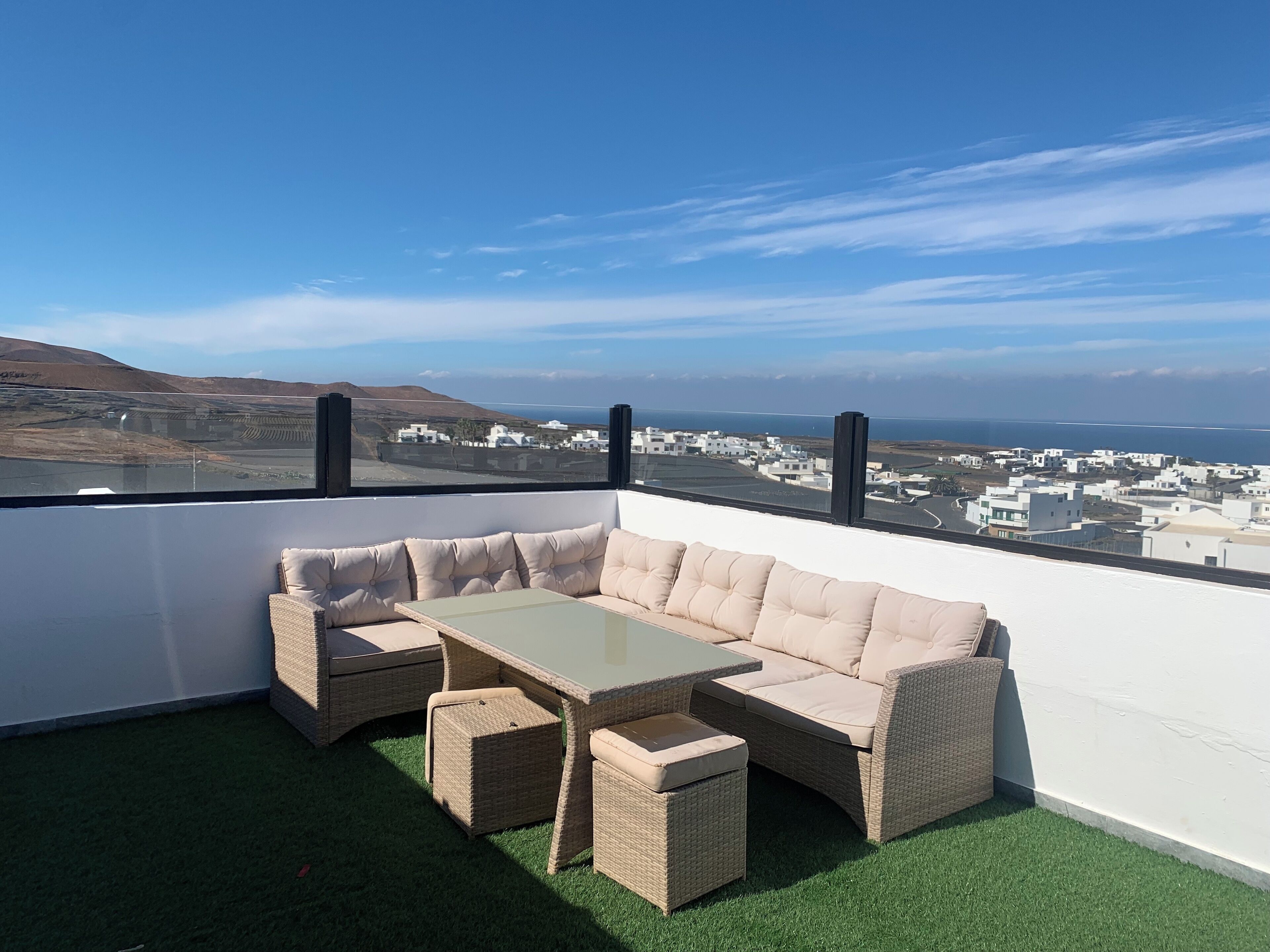 Un balcón con sofá y mesa de mimbre, con vistas a un pueblo costero.