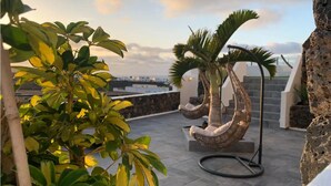 Una terraza en la azotea con un muro de piedra, una palmera y una escultura espiral original.