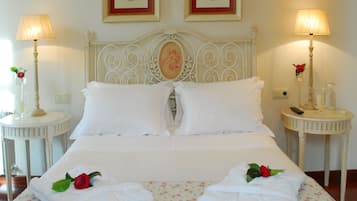 A neatly made bed with white linens and floral-patterned bedding, flanked by two bedside tables with lamps and framed pictures above.