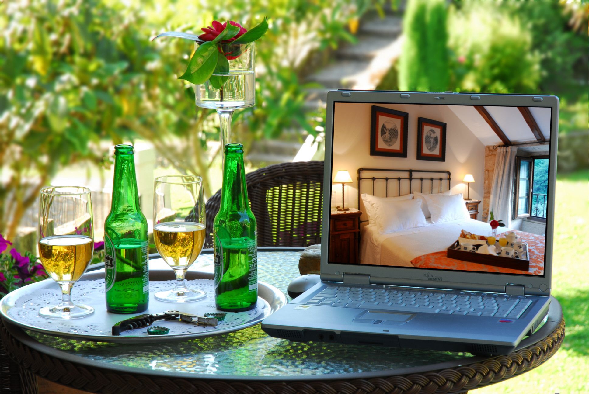 A laptop on a table with a tray of drinks and a bottle of beer.