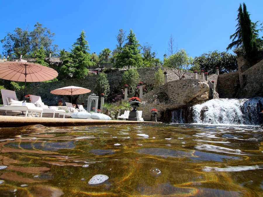 Un espace piscine agrémenté de chaises longues et de parasols, une cascade et une végétation luxuriante.