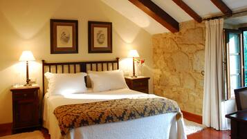 Une chambre à coucher avec un lit, deux lampes de chevet, un mur en pierre et une fenêtre avec des rideaux.