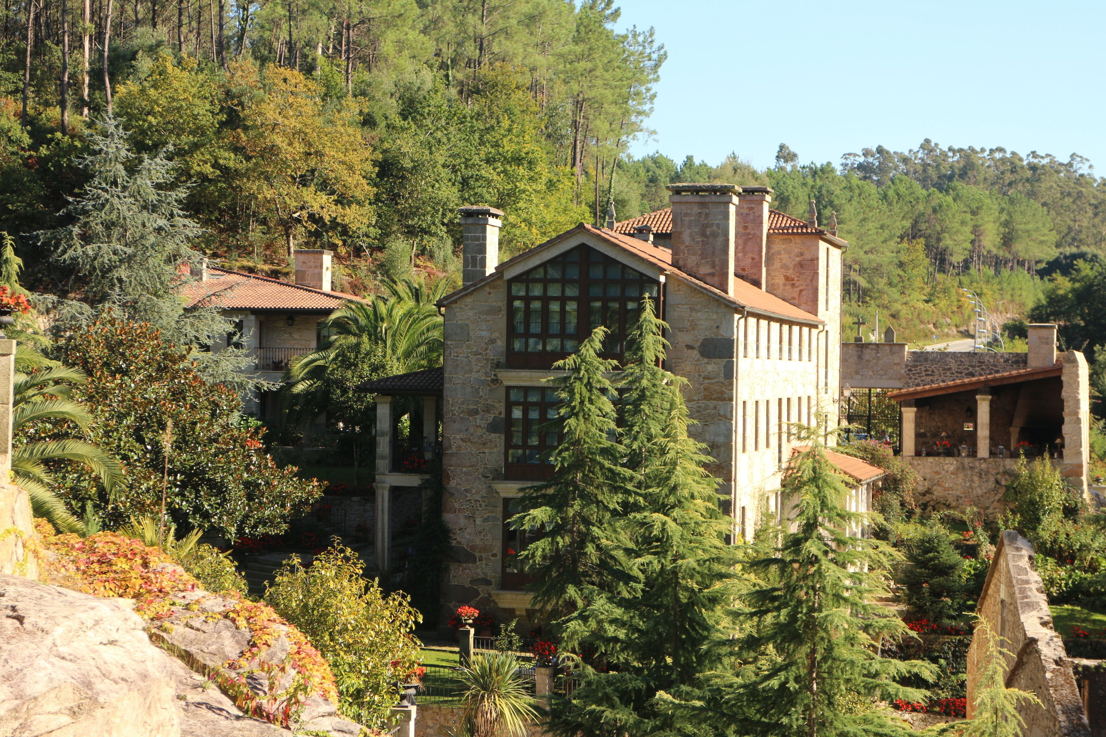 A stone building with a tiled roof, surrounded by lush greenery and trees.