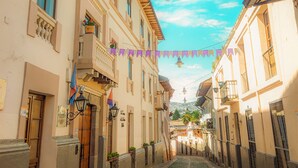 Una calle adoquinada flanqueada por edificios con balcones, un cielo azul despejado y luces colgantes.