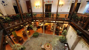 Un amplio patio interior con una mesa redonda central rodeada de sillas, plantas en macetas y una zona de estar con sofás y una mesa de centro.