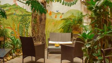 Un patio al aire libre con mobiliario de mimbre, plantas en macetas y un mural en la pared.