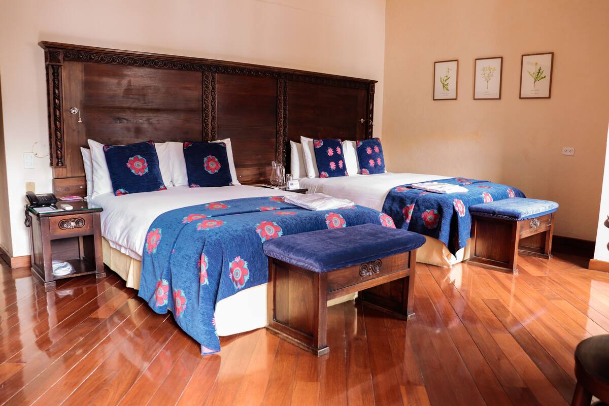 Habitación de hotel con dos camas, cabecero de madera y un banco.