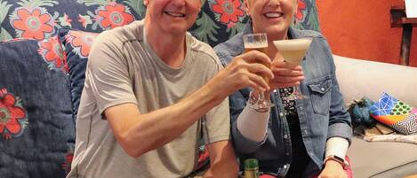 Twee personen zitten op een bank met een bloemenprint, met drankjes in hun handen.