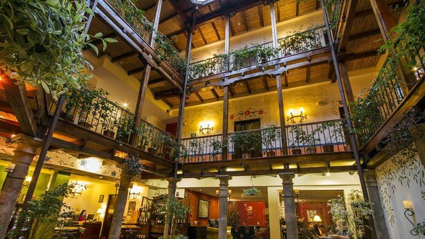 Un atrio de varios niveles con balcones de madera, plantas en macetas y un espacio central abierto con asientos.