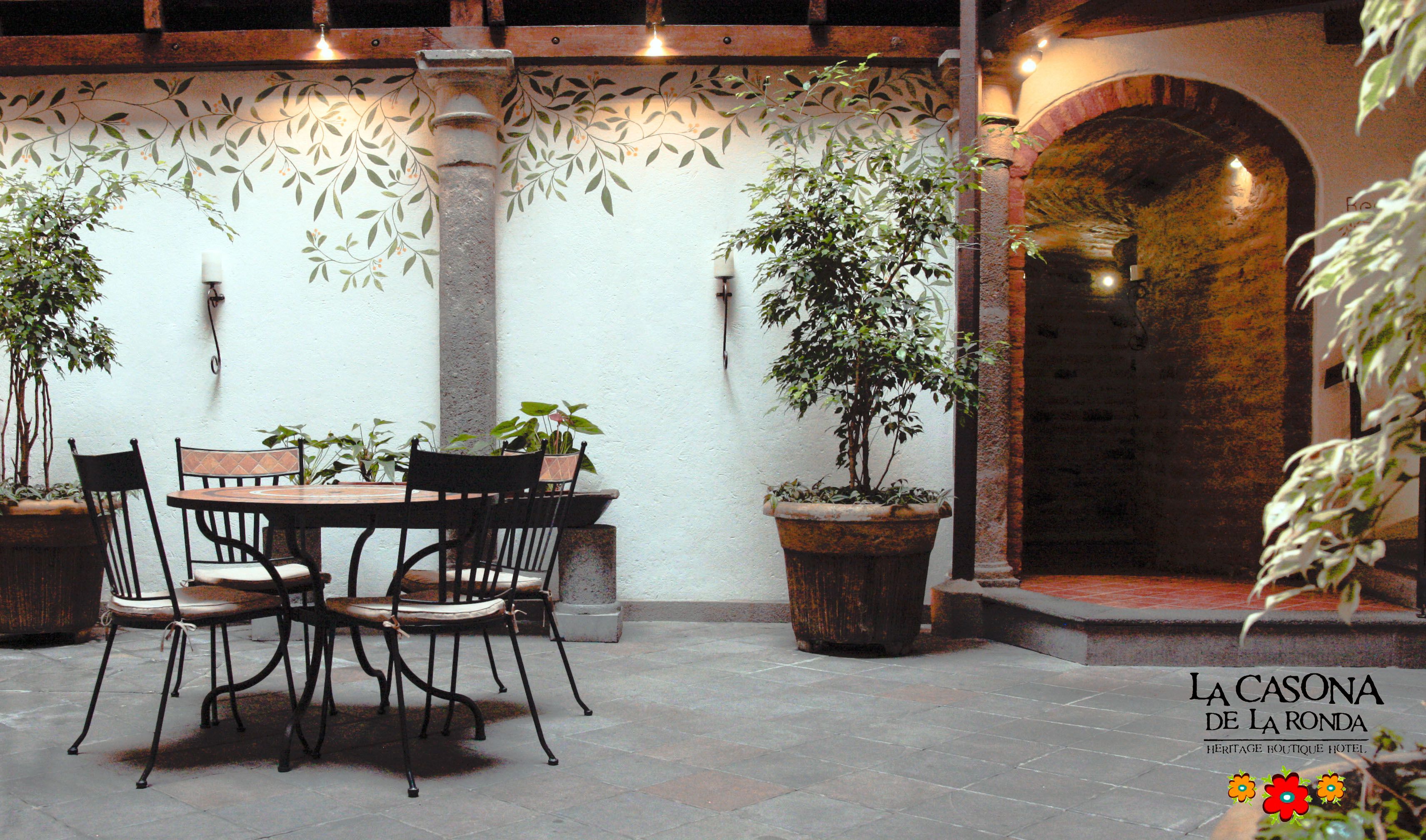 An outdoor patio with a table and chairs, surrounded by potted plants and a decorative wall.