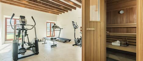 A gym with various exercise machines, a wooden sauna, and a large window.