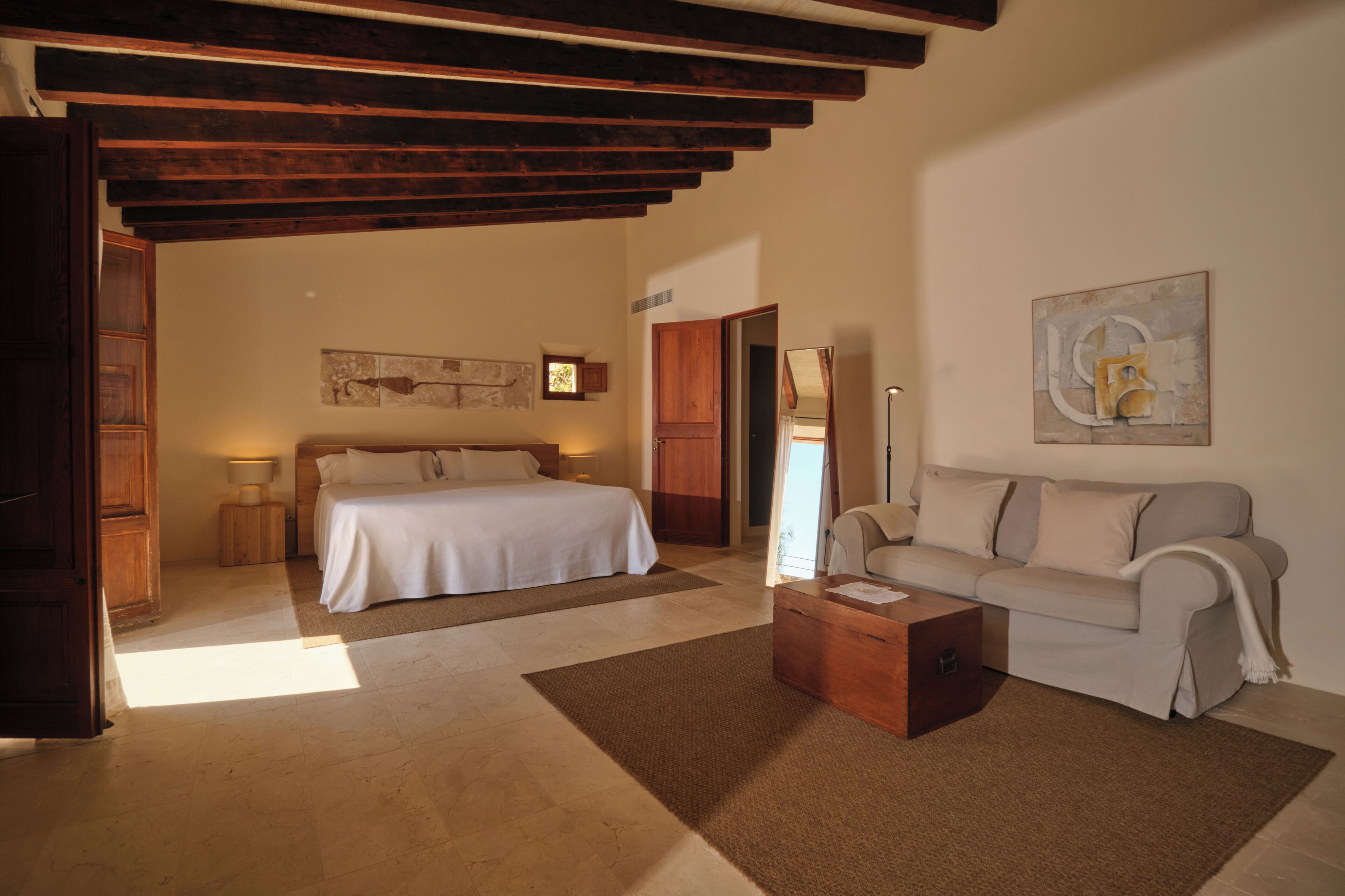 A bedroom with a bed, a sofa, a coffee table, and a painting on the wall.