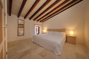 Un dormitorio con una cama grande, vigas de madera en el techo, una mesita de noche con lámpara y un espejo en la pared.