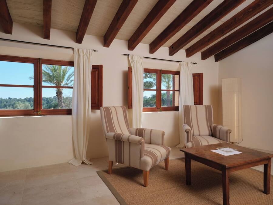 Una habitación con dos sillones, una mesa de madera y ventanas amplias con cortinas.