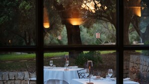 An outdoor dining area with tables set for two, each with a white tablecloth, wine glasses, and candles.