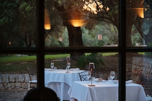 Un espace de restauration en plein air avec des tables préparées pour deux personnes, chacune agrémentée d’une nappe blanche, de verres à vin et de bougies.
