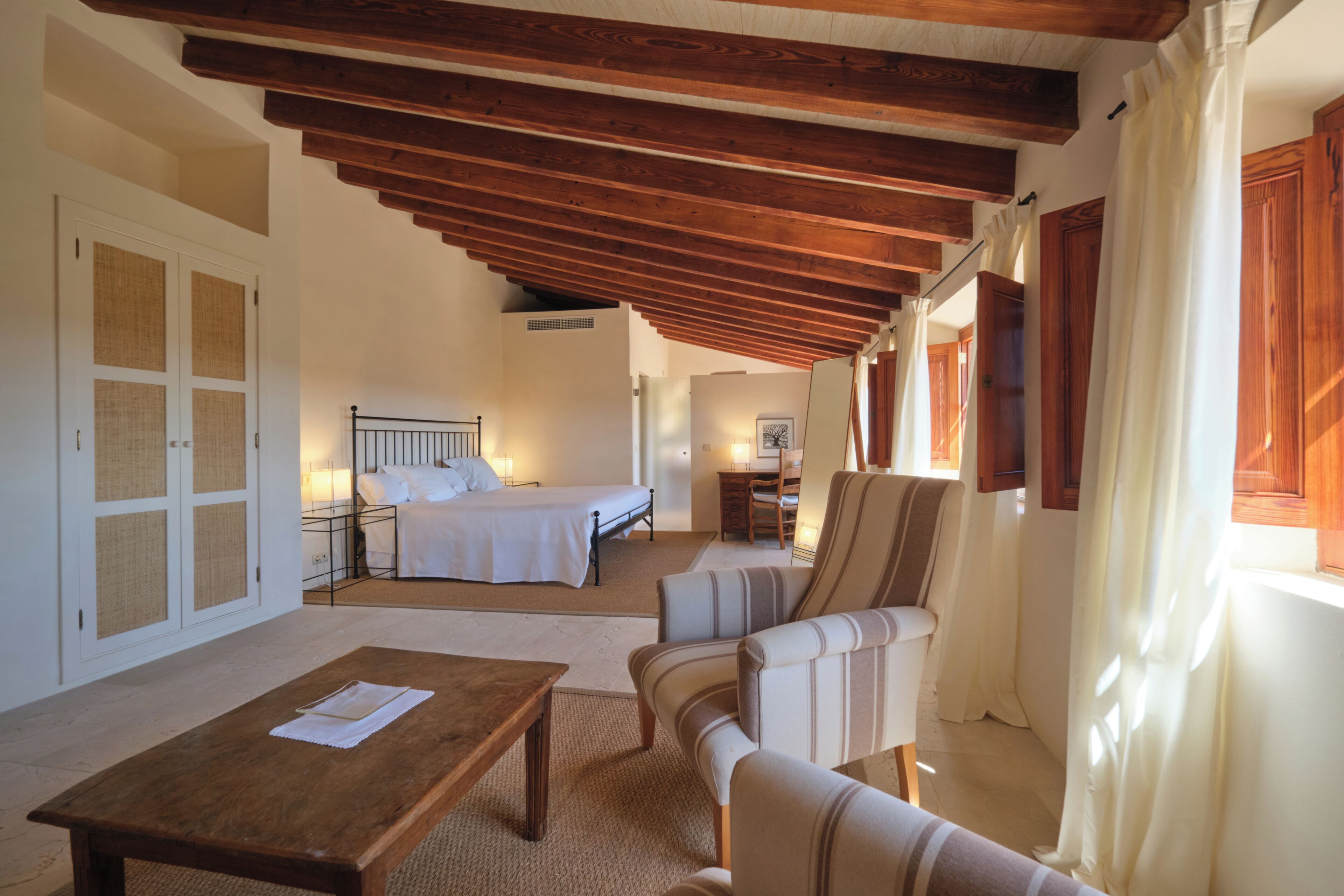 Um quarto com cama, mesa de madeira, cadeira e janela com cortinas.