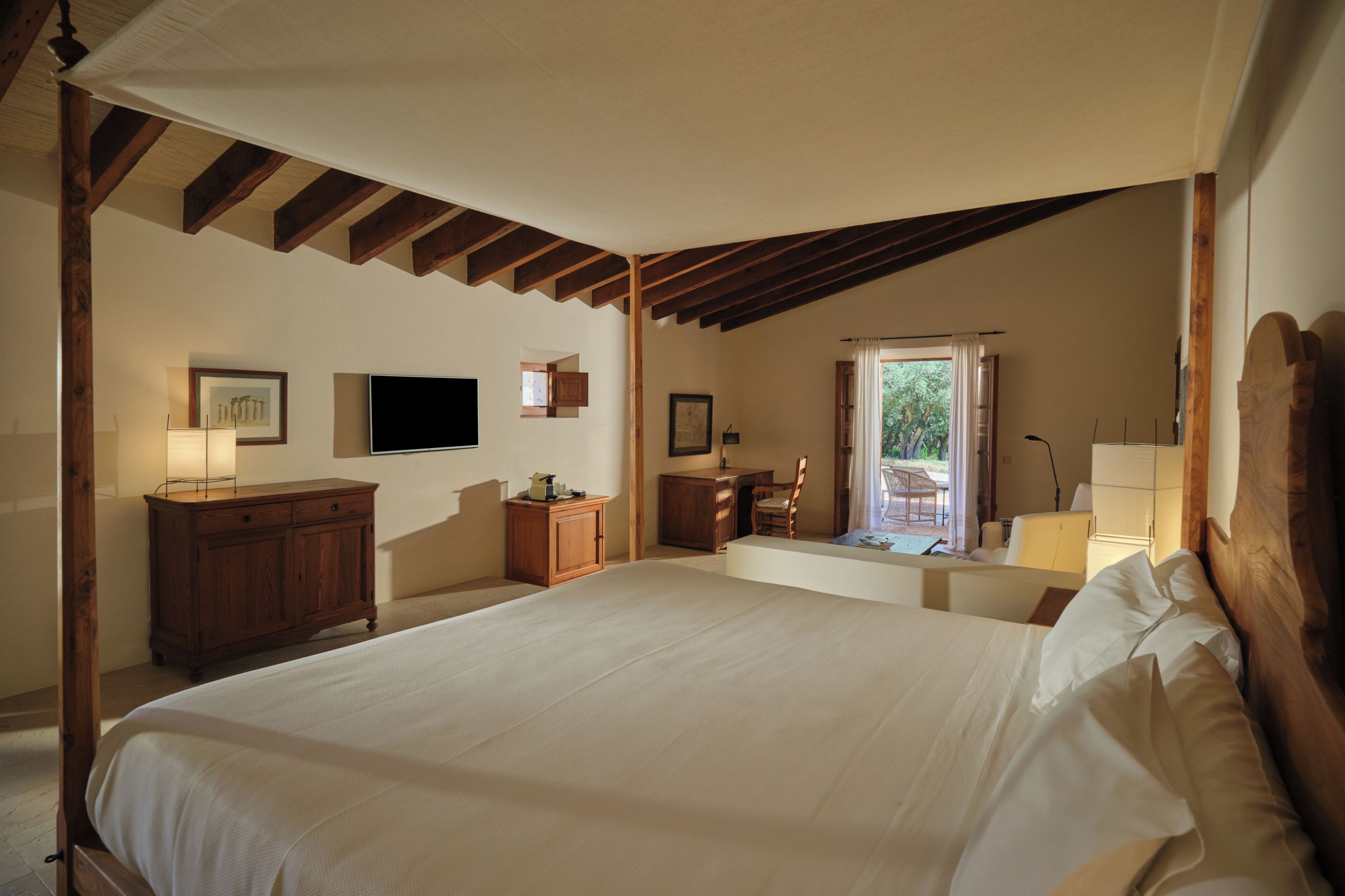 A bedroom with a large bed, wooden beams, a desk, a chair, a television, and a window with curtains.