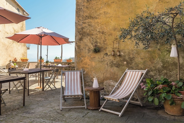 An outdoor patio with striped lounge chairs, wooden tables, and red umbrellas. - Corte Paganini (Ricco del Golfo di Spezia)