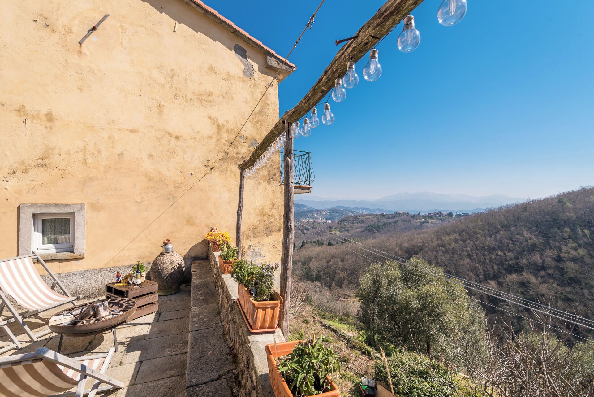 A rustic terrace with outdoor seating, a small window, and a view of a hilly landscape.