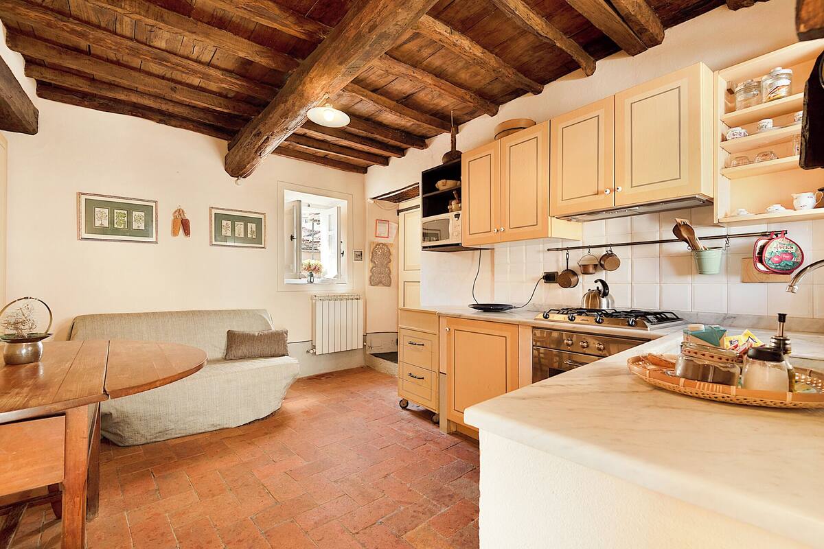 Una cocina rústica con vigas de madera, una zona de comedor con sofá y un radiador.