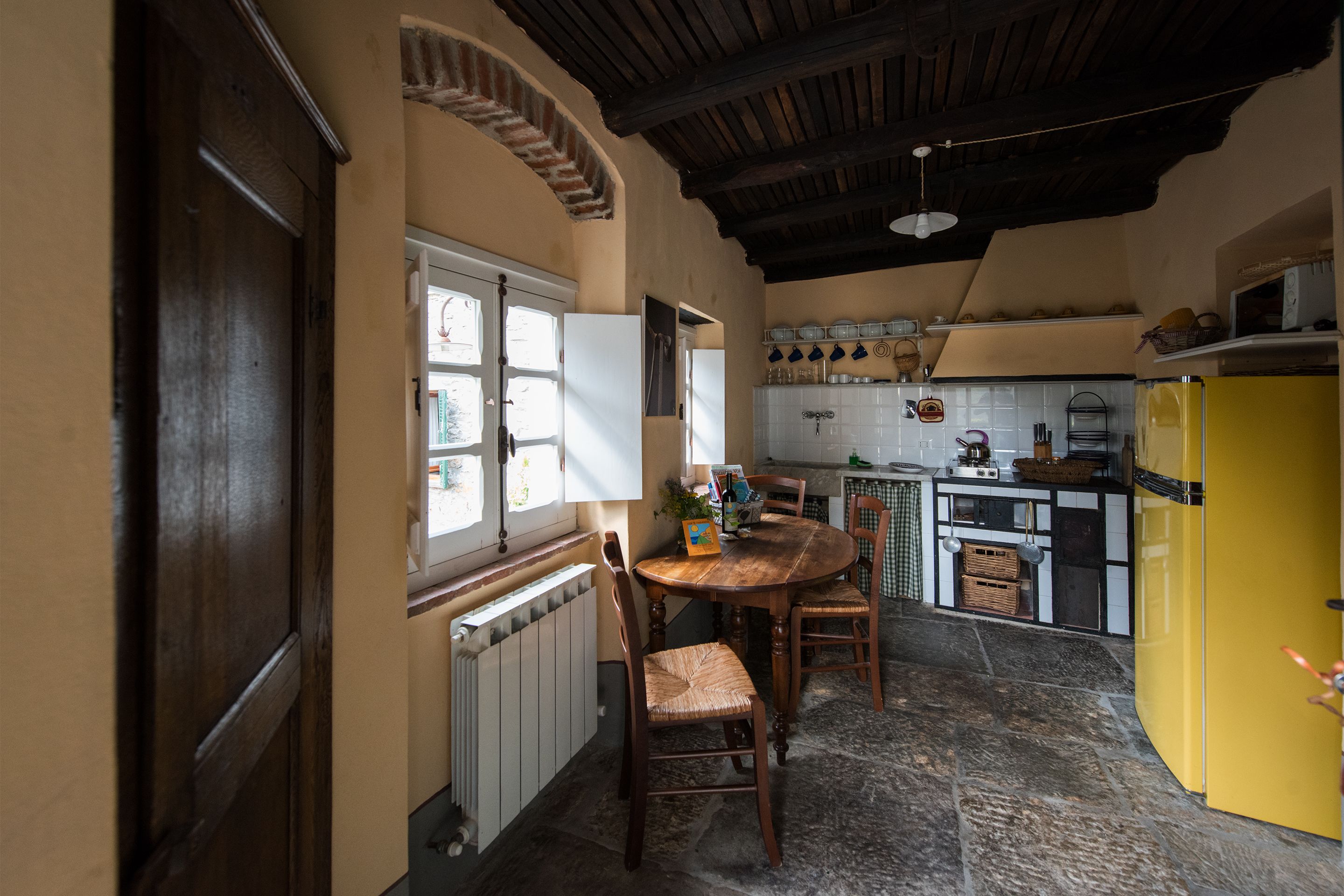 Una cucina con un tavolo di legno, sedie, un frigorifero giallo e una finestra con tende.
