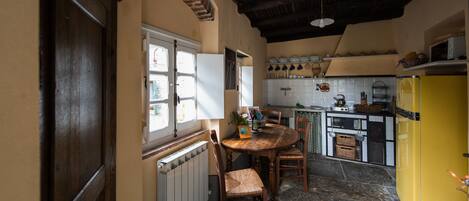Una cucina con un tavolo di legno, sedie, un frigorifero giallo e una finestra con tende.