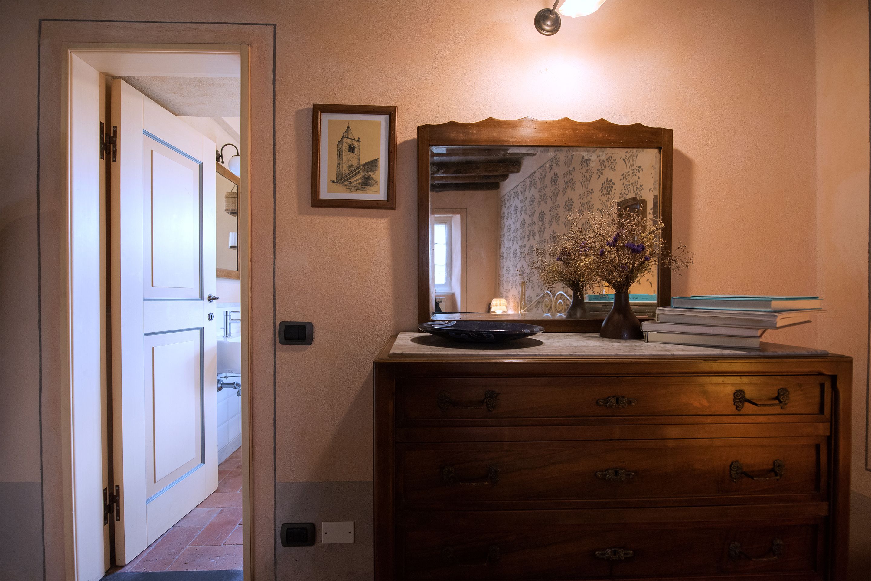 A hallway with a wooden dresser, a mirror, and a vase with flowers.