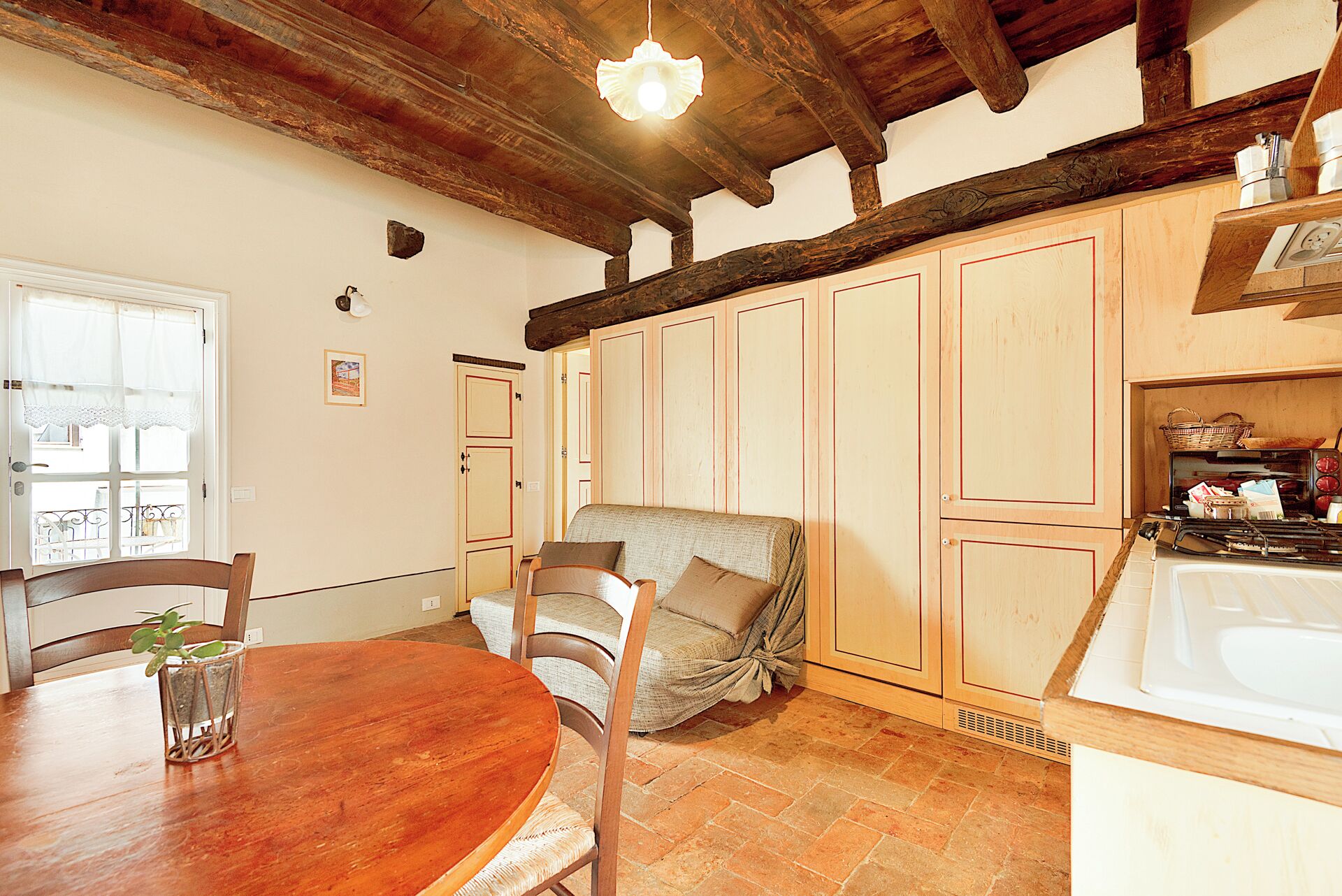 A rustic kitchen with wooden cabinets, a dining table with chairs, and a hanging light fixture.