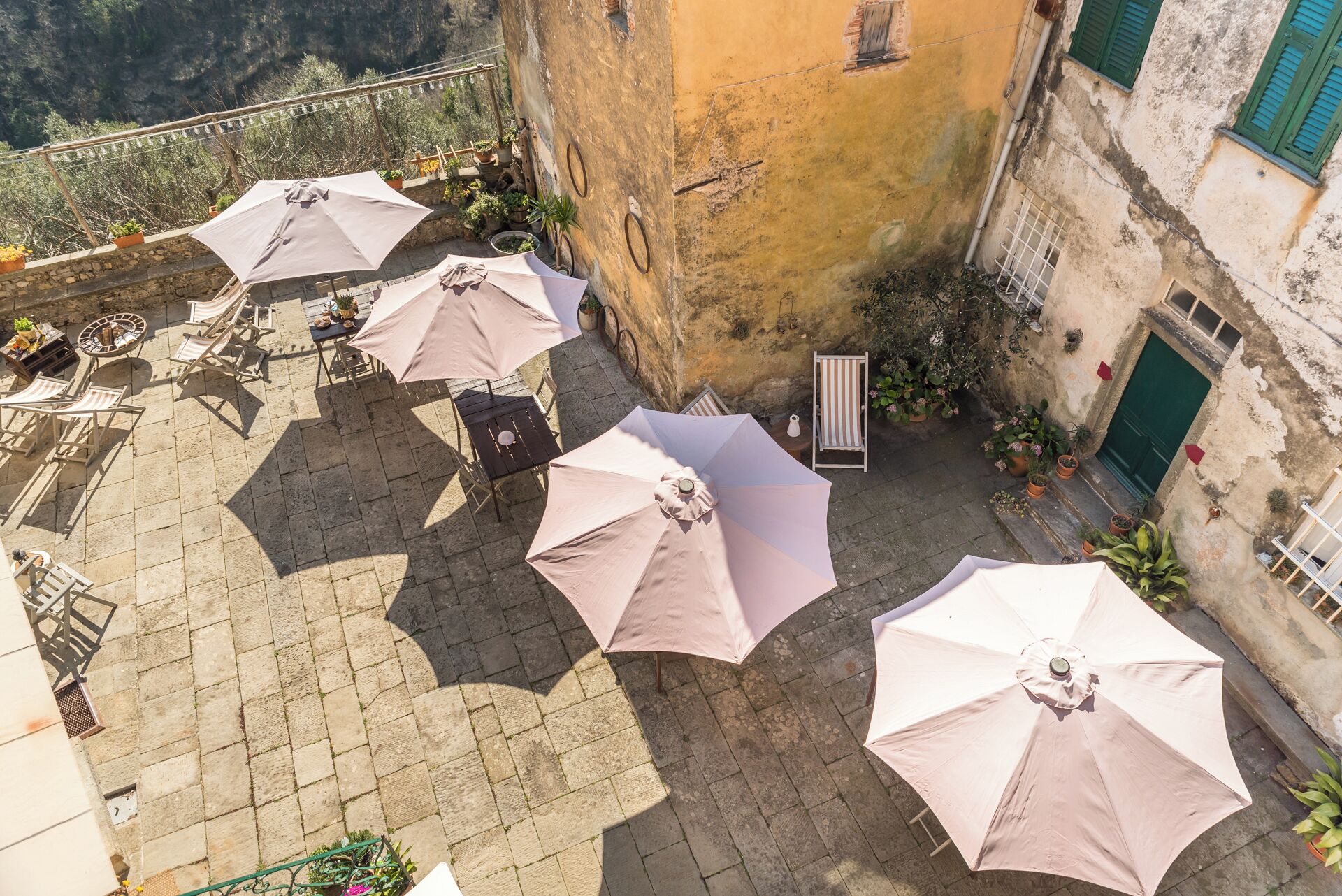 An outdoor patio with multiple tables and umbrellas, surrounded by stone walls and potted plants.