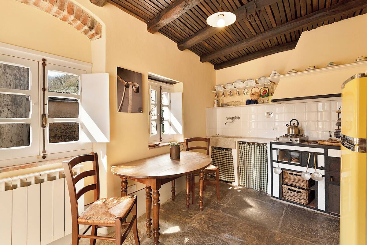 Una cocina con una mesa de madera, sillas, una estufa y un ventanal con vistas a árboles.