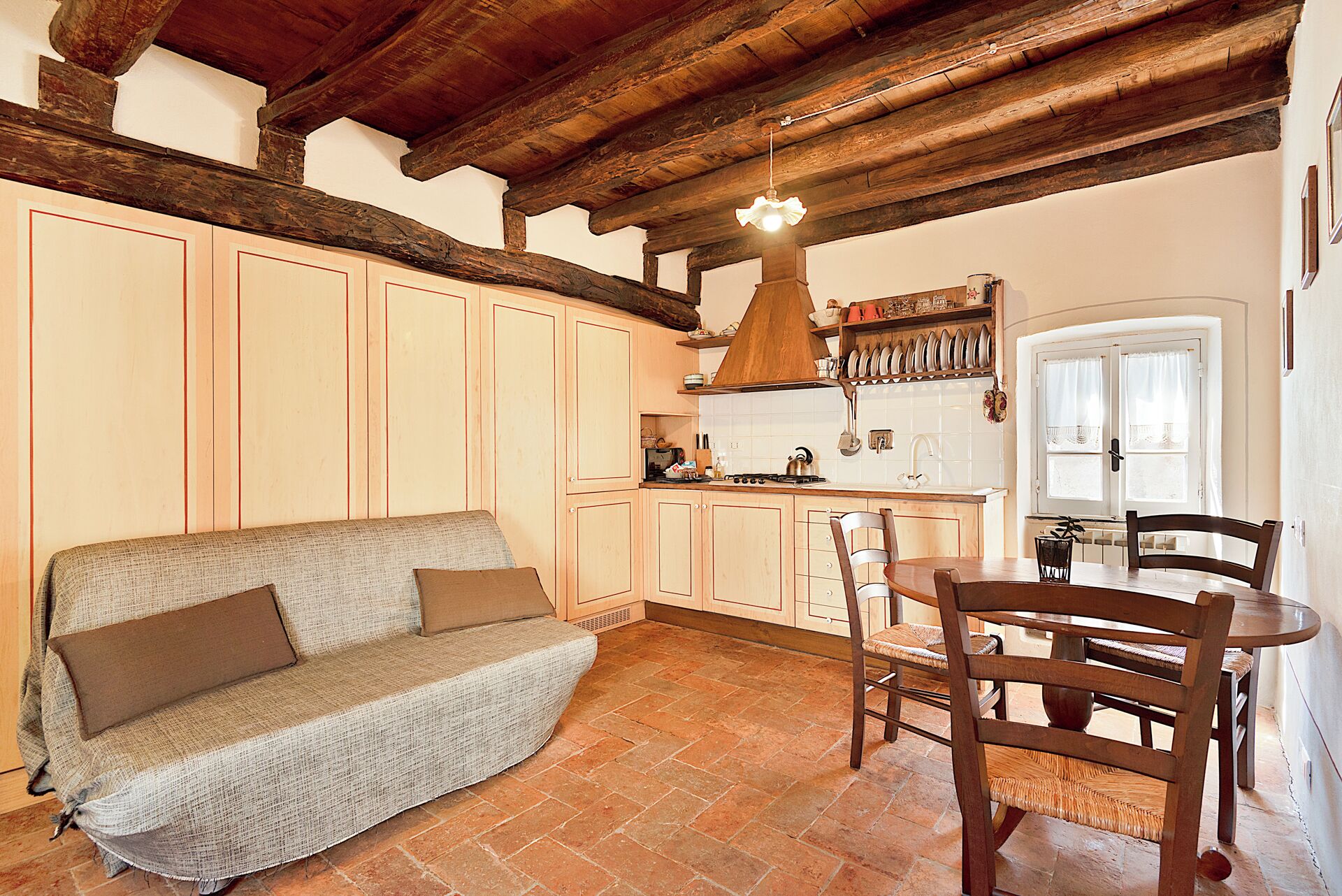 A cozy kitchen with wooden cabinets, a dining table with chairs, and a sofa.
