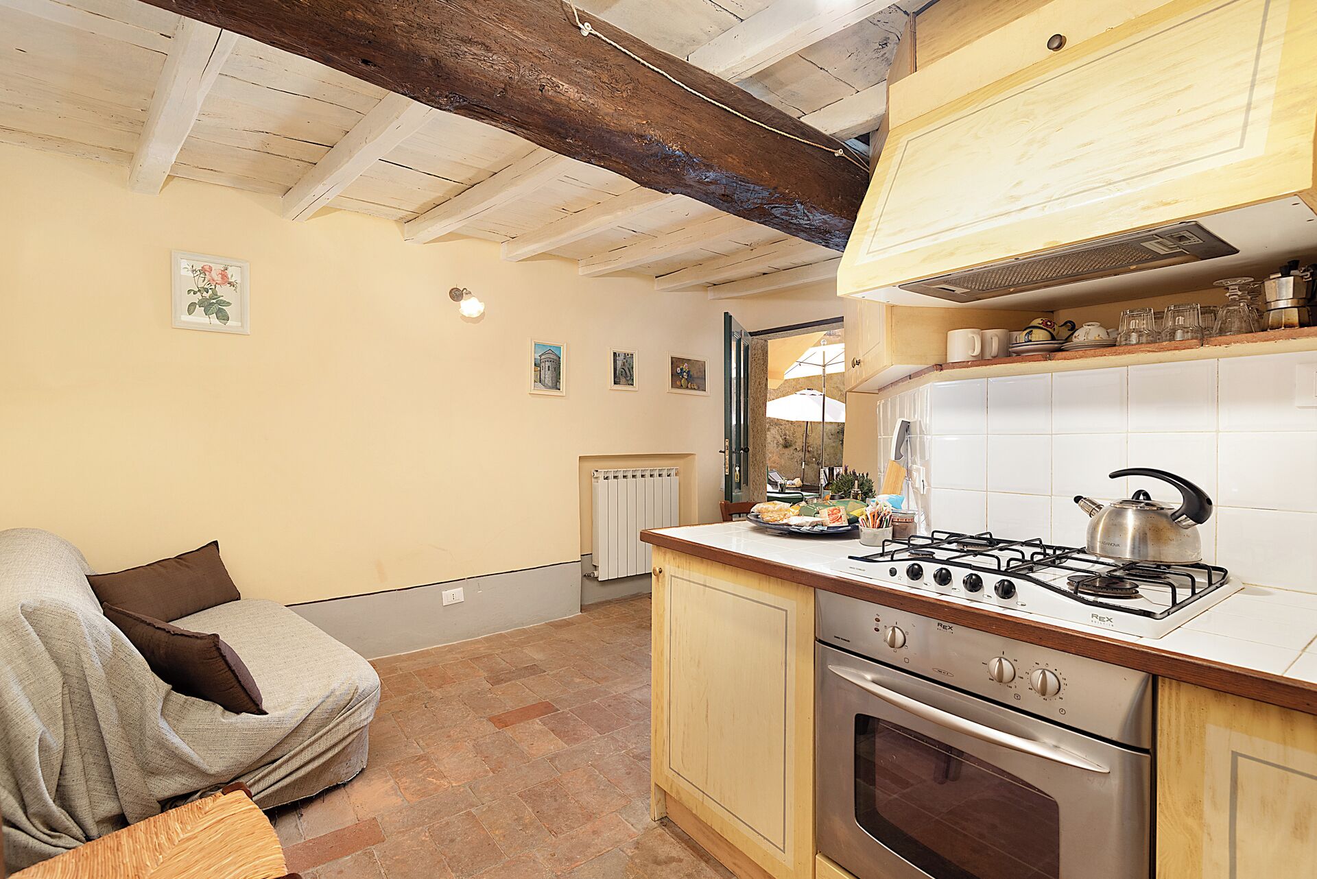 A cozy kitchen with a wooden ceiling, a stove, and a dining area with a chair and table.